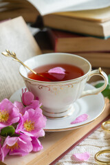 A cup of aromatic tea, a book and a rose on the table.