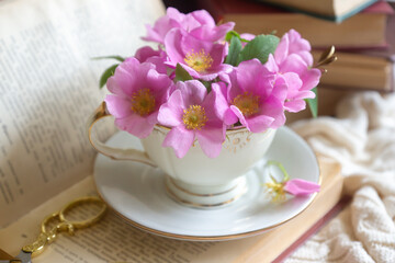 A cup of aromatic tea, a book and a rose on the table.