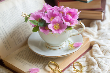 A cup of aromatic tea, a book and a rose on the table.