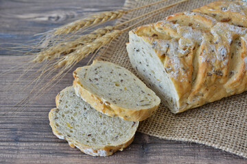 Sliced loaf of artisan bread with seeds and wheat stalks on a rustic wooden surface