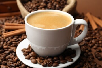 Cup of hot coffee, beans and cinnamon on brown background, closeup