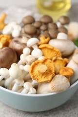 Different raw mushrooms in bowl on grey textured table, closeup