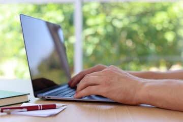 Man working on laptop at wooden table indoors, closeup
