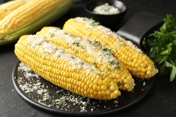 Tasty grilled corncobs with parsley and cheese on black table, closeup