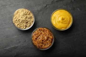 Different types of mustard on black table, flat lay