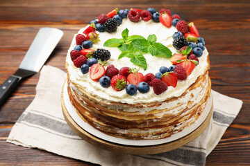 Delicious crepe cake with fresh berries and server on wooden table, closeup