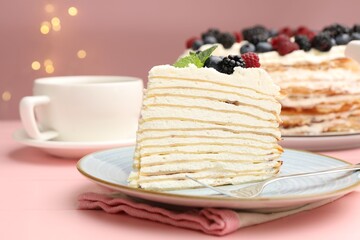 Piece of tasty crepe cake with berries served on pink wooden table against blurred lights, closeup