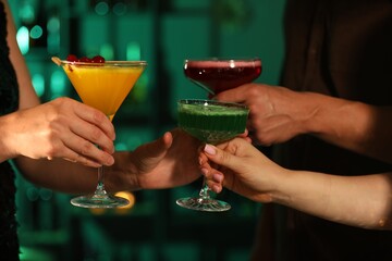 Friends clinking glasses with cocktails in bar, closeup