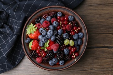 Different ripe berries in bowl and napkin on wooden table, top view