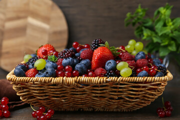 Different ripe berries in wicker basket on wooden table, closeup