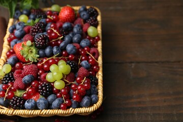 Different ripe berries in wicker basket on wooden table, closeup. Space for text