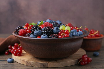 Different ripe berries in bowl on wooden table against brown background, closeup