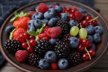 Different ripe berries in bowl on wooden table, closeup