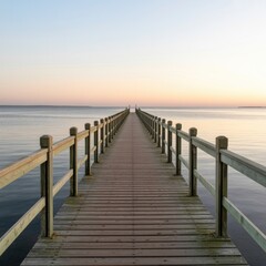 Fototapeta premium A long wooden pier stretching out into calm water under a pastel sky at sunset or sunrise