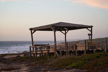 Wooden gazebo on the coast of Portugal. Waves, cliffs, pastel sky, peaceful scene, natural depth, sunset atmosphere, viewing platform.