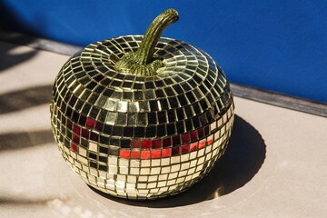 Golden Mirror Mosaic Pumpkin Decoration in Sunlight. Reflective golden pumpkin made of mirror tiles sitting in sunlight with bold shadows, creating a modern and festive aesthetic
