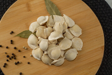 Frozen dumplings semi-finished product piled up decorated with spices on a board top view