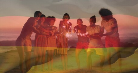 Naklejka premium Eight friends leaning on sandy beach at sunset over ocean horizon, with handheld sparklers glowing