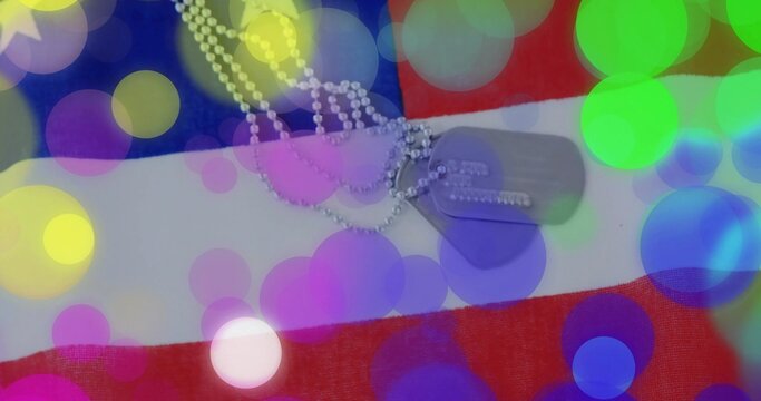 Fototapeta Displaying military dog tags on ball chain lying flat on American flag, with colorful bokeh overlay
