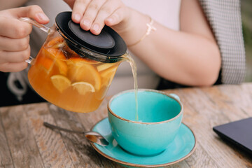 A woman pours hot  sea buckthorn (or citrus ) tea with ginger into a blue cup in a cafe . Health and comfort 