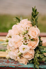 A delicate wedding bouquet with soft pink roses and green leaves on a rustic wooden bench.