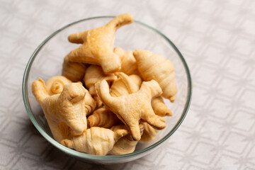 Mini croissants and cat shaped cookies in glass bowl on patterned tablecloth, top view