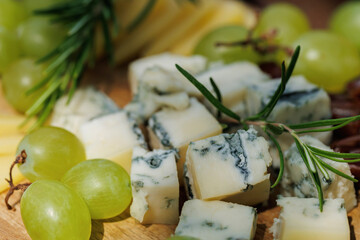 Detailed view of blue cheese, green grapes and fresh rosemary on rustic wooden board..