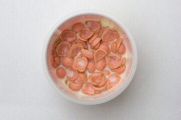 A bowl of pinky colored crispy corn flake cereal with milk isolated on white background.