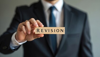 Obraz premium Businessman holds wooden block with the word revision. The photo shows a business person wearing a suit and tie. Concept about review or update in business or finance.