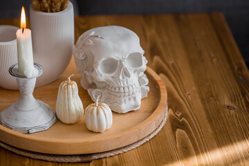 Halloween celebration. A white skull, candles and pumpkins on the table. Decor for the Day of the Dead or Halloween in the living room interior.