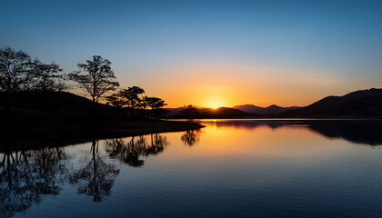 Naklejka premium Serene Sunset Over A Calm Lake With Silhouetted Trees And Hills
