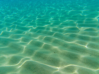 Clear underwater view of sandy seabed with sunlight reflections