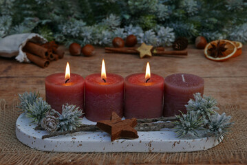 Third Advent: Decoration with rust-colored candles, cinnamon sticks, orange slices, and nuts in front of fir branches with space for text.