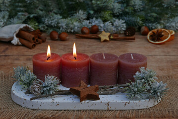 Second Advent: Decoration with rust-colored candles, cinnamon sticks, orange slices, and nuts in front of fir branches with space for text.