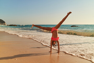 Young girl performs a handstand on sandy beach at sunset near the ocean
