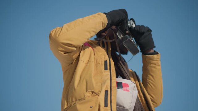 lower view of shutterbug adjusting lens on retro camera, gloved fingers fine tuning focus ring then pressing shutter trigger to capture crisp winter urban scene under bright sun