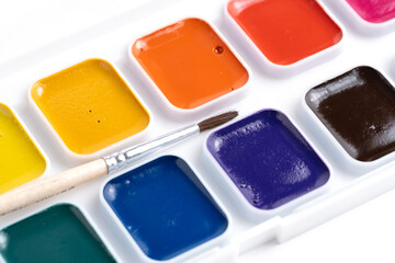 Watercolor paints and brush stand out against white background, closeup.