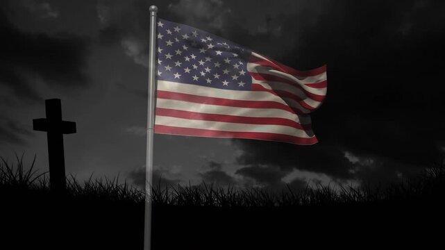 Rising breeze unfurling US flag on metal pole above grass-and-cross silhouette under dusk sky