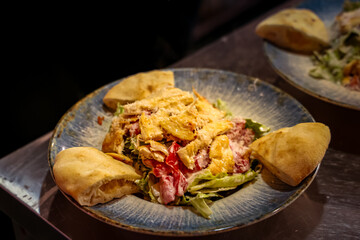 Caesar salad with grilled chicken, fresh lettuce, tomatoes, parmesan cheese, creamy dressing, and warm bread pieces served on a rustic plate.
