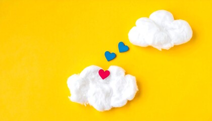 Two fluffy white clouds float against a bright yellow backdrop, adorned with small red and blue hearts, suggesting a cheerful and whimsical scene.
