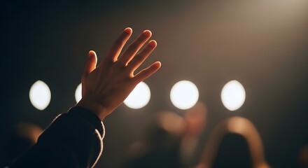 Hand raised in worship with blurred lights in the background.