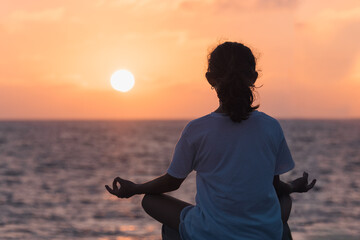 Young woman meditate at sunset over the sea.