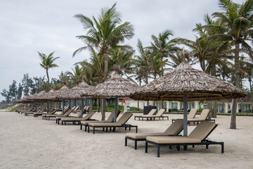 Row of deck chairs under a palm umbrella in beautiful Cua Dai Beach in Hoi An, Central Vietnam
