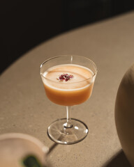 Orange colour cocktail in a stem glass kept on a marble table