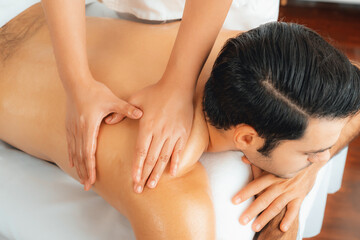 Fototapeta premium Caucasian man customer enjoying relaxing anti-stress spa massage and pampering with beauty skin recreation leisure in day light ambient salon spa at luxury resort or hotel. Quiescent