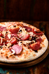 Pizza with ham, salami, cherry tomatoes and mozzarella cheese. Rustic wooden background. Soft focus. Close up.	
