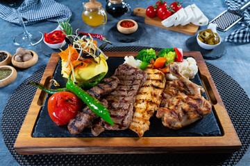 Mixed grilled meat with vegetables and mashed potatoes on wooden plate
