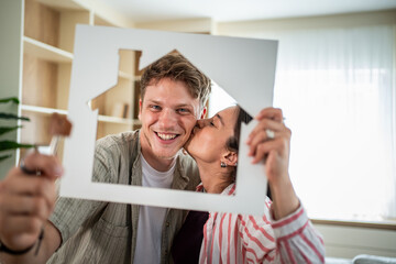 Happy couple kissing and holding house frame symbolising new home