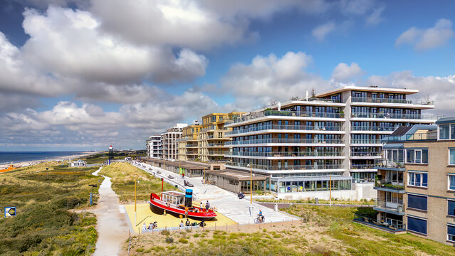 A vibrant, red play boat sits on a sandy playground near a modern residential area by the sea at Kijkduin in The Hague. The scene is bright and inviting, with families enjoying the coastal view.