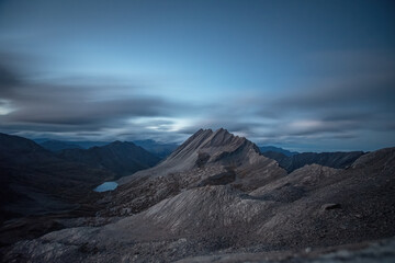 Crête de la Taillante (Taillante crest) stands out against the dramatic sky of a summer evening, with the Foréant lake illuminated by the last light at its foot. Cottian Alps. 